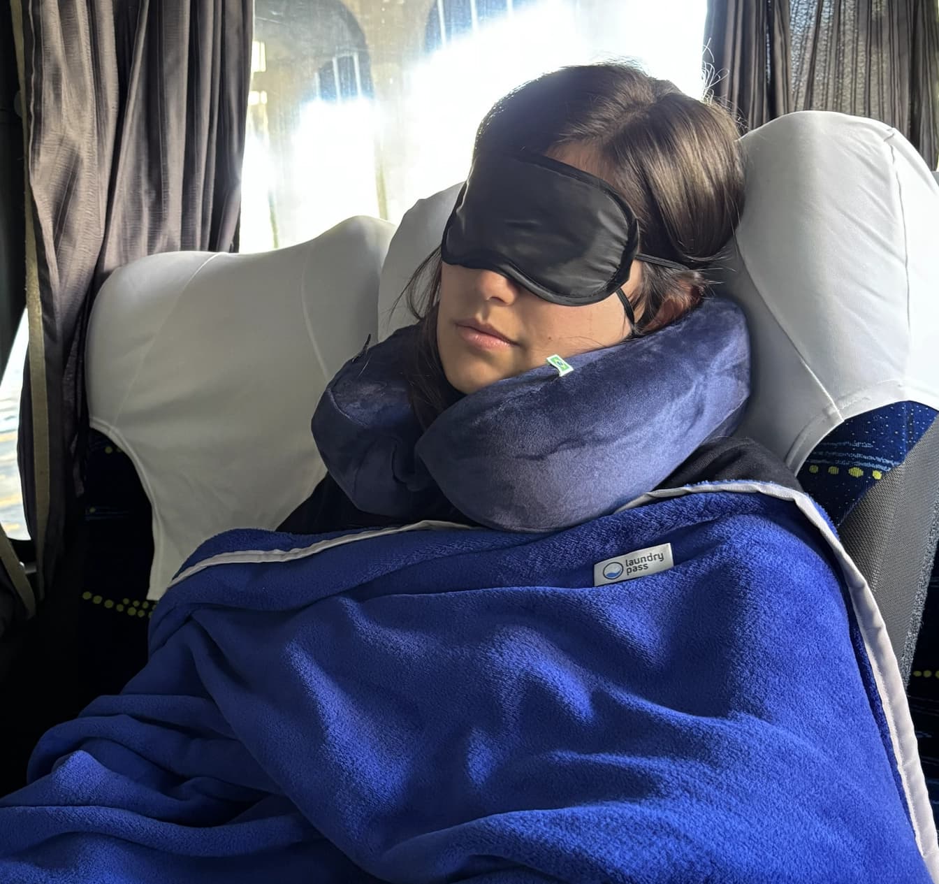 Pessoa descansando no ônibus com kit de conforto: manta, pescoceira e tapa-olho